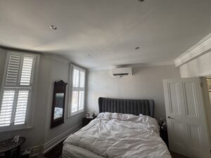 Wall-mounted air conditioning unit installed above the bed in a Teddington bedroom